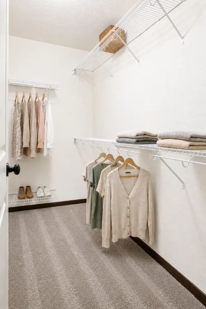 Walk-in closet with neatly hung clothes, folded items on shelves, and shoes on the floor.
