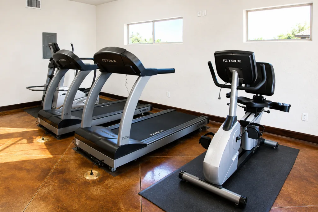 A gym with two treadmills and a stationary bike on brown flooring near a white wall.