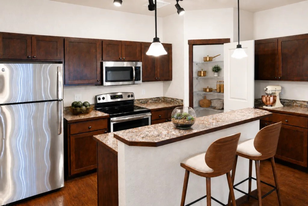 A modern kitchen with dark wood cabinets, a stainless steel fridge, and a granite island with two bar stools.