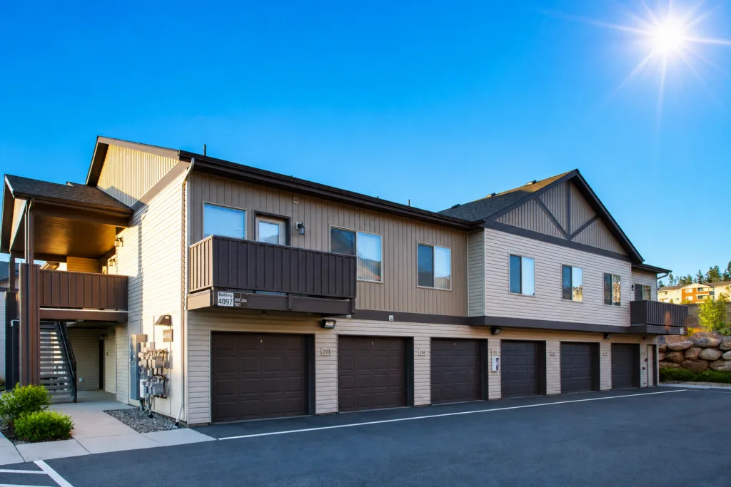 A two-story residential building with garages on the ground floor and a clear, sunny sky above.
