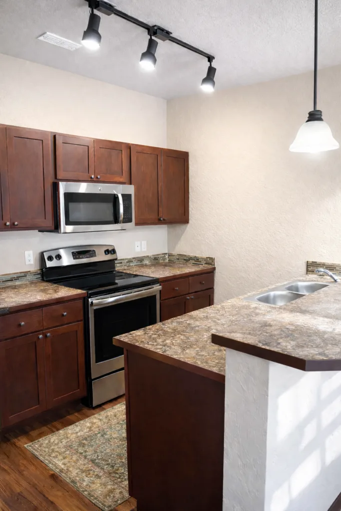 Modern kitchen with dark wood cabinets, stainless steel appliances, granite countertops, and a double sink under track lighting.